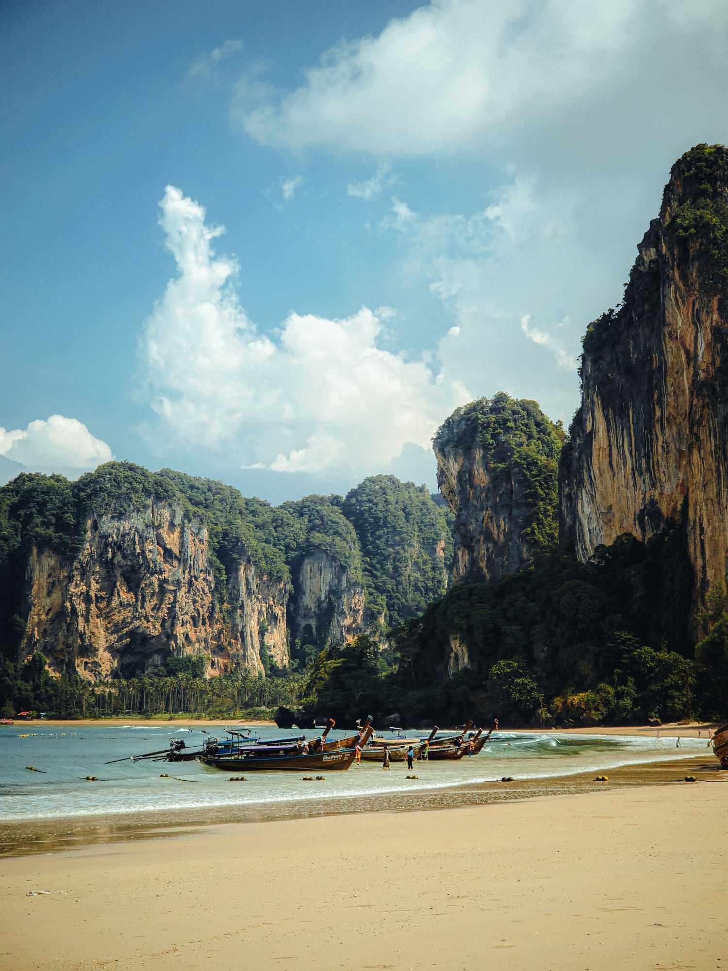 Longtail boats moored on a quiet beach below limestone cliffs in southern Thailand