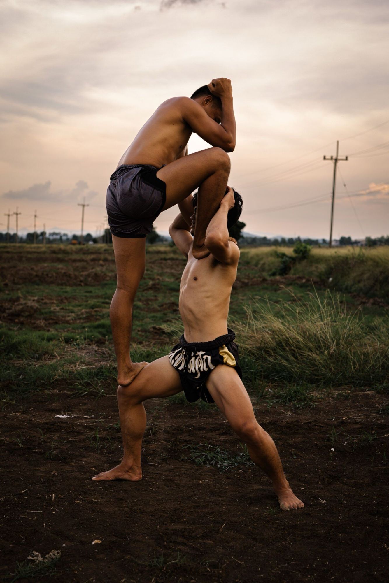 Two men doing a partner leg stretch in an open field in Thailand