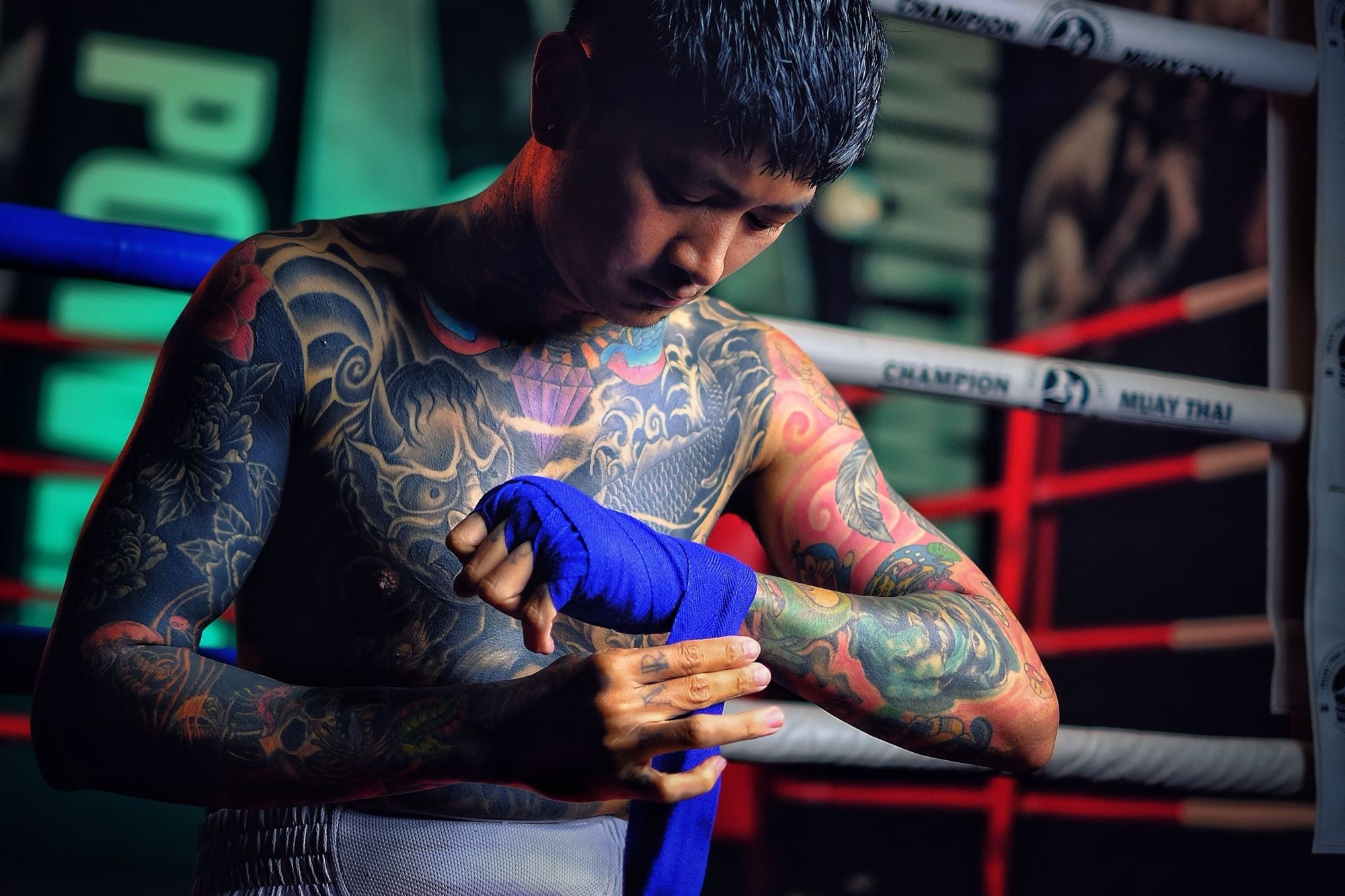 A Muay Thai student wrapping his hands with blue wraps beside the ring