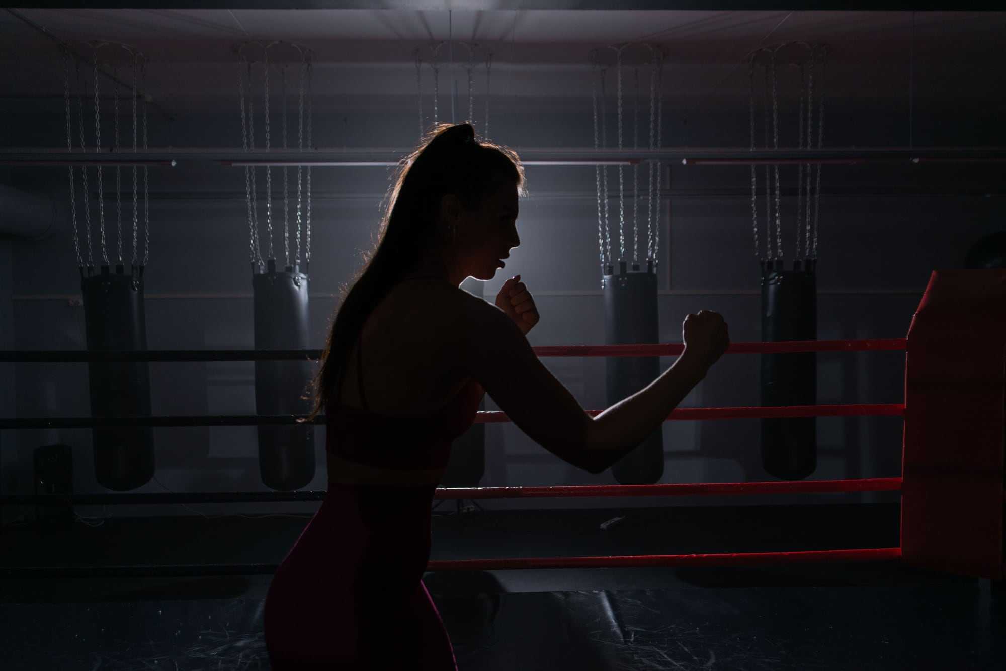 A woman shadow boxing in a quiet gym, in silhouette