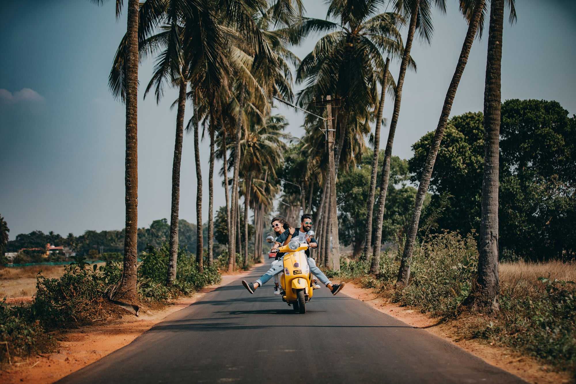 Two people on a scooter on a quiet palm-lined road