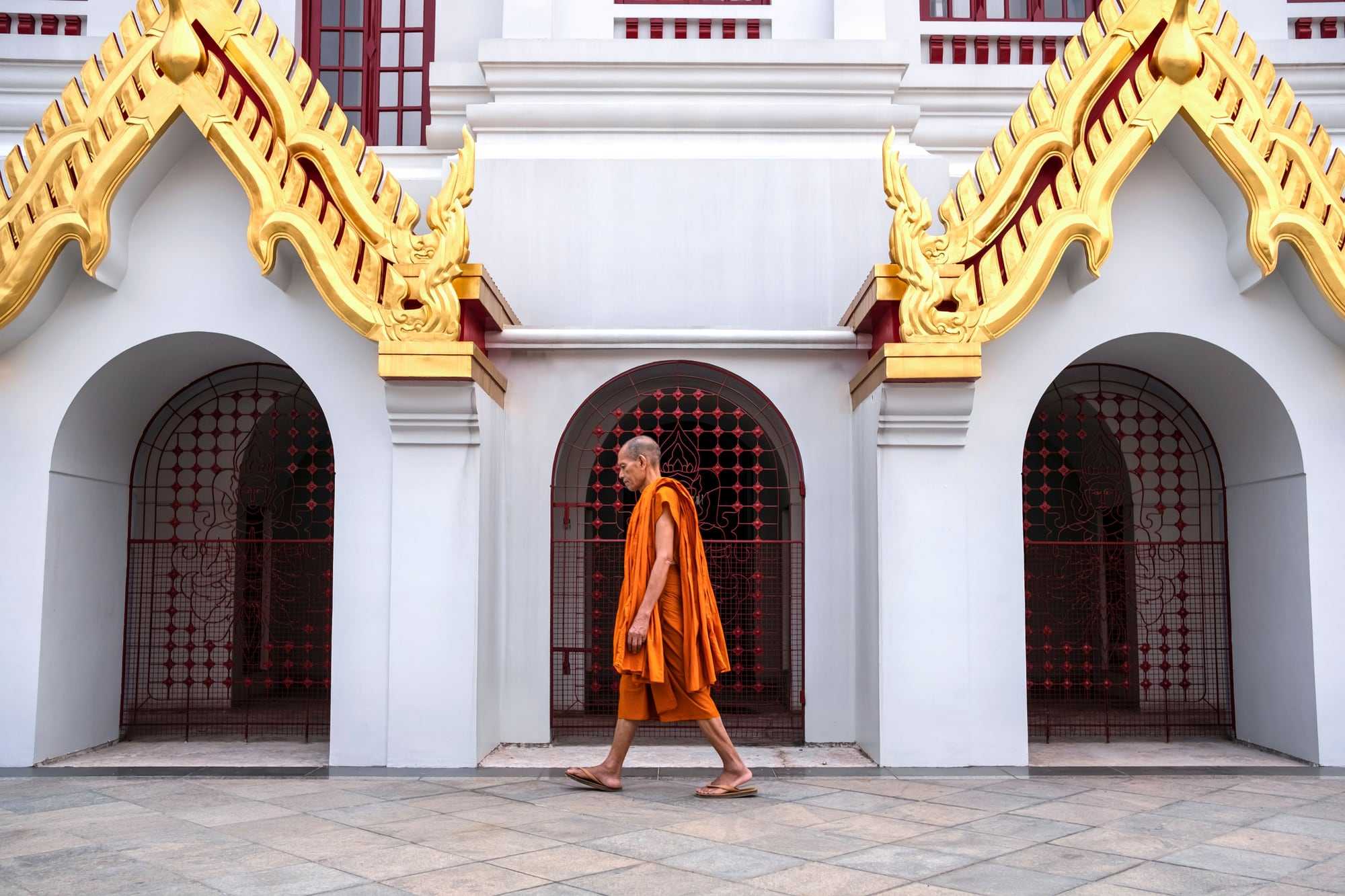 A monk in an orange robe walking past a white and gold temple building