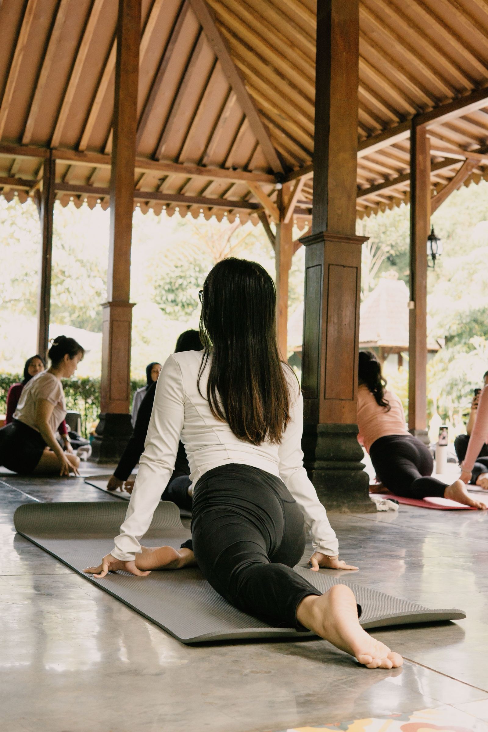Students in a group yoga class in an open-air wooden pavilion surrounded by greenery in West Java, Indonesia